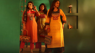 Three women in traditional outfits standing in a room with a green wall.